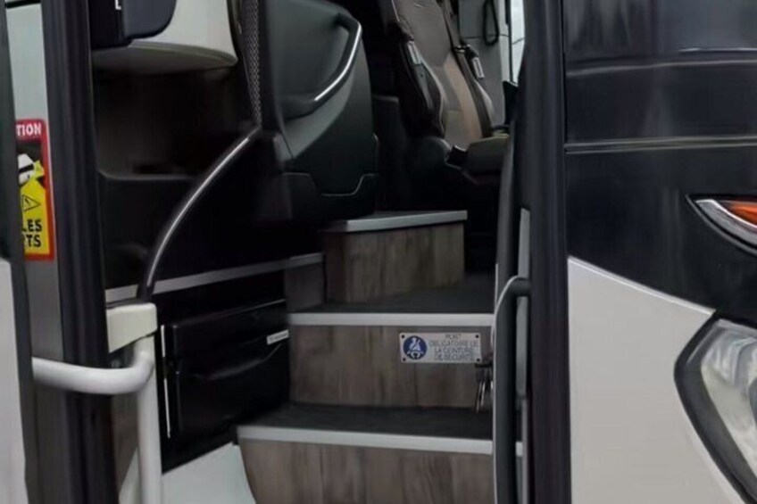 A bus interior with steps leading to the driver's seat, a caution sign, and a wheelchair accessibility symbol. 4