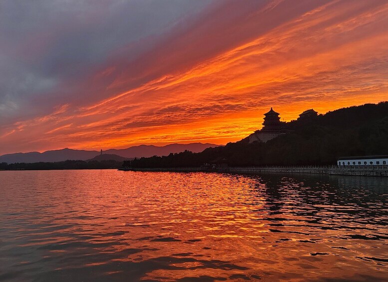 A sunset over a calm lake with a pagoda and mountains in the background. 2
