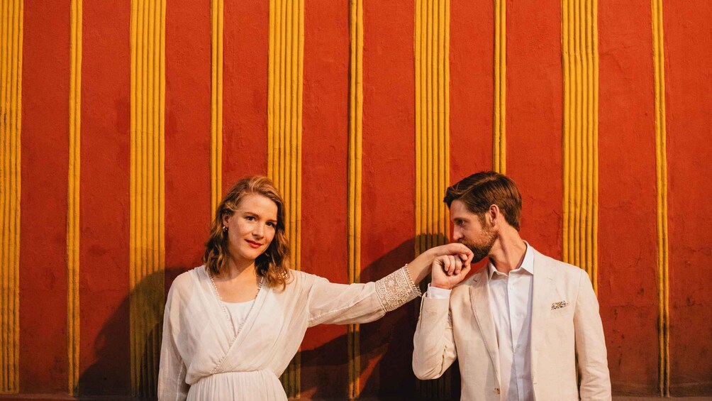 A couple standing in front of a red wall with yellow vertical stripes. 2