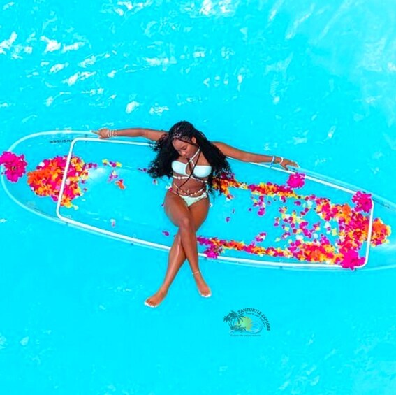A person in a bikini holding a surfboard in a pool with colorful flower petals. 1
