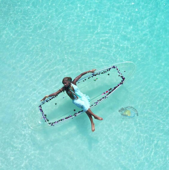 A person floating on a clear blue body of water, wearing a white dress and a gold necklace. 5