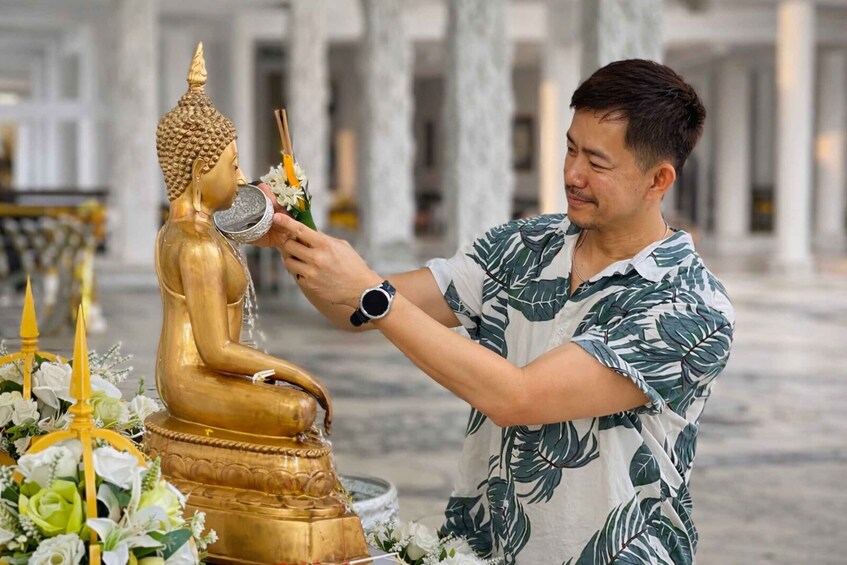 Une personne effectue un rituel devant une statue de Bouddha en or, entourée de fleurs et de bougies. 3