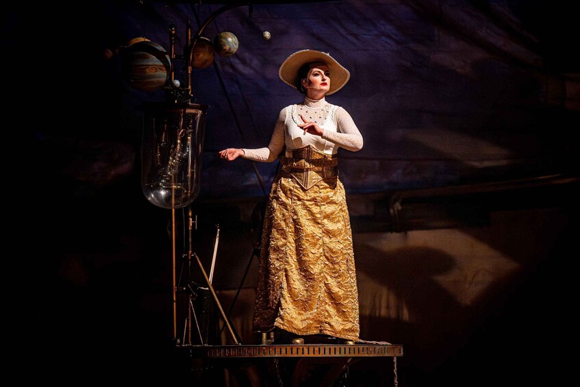 A person on stage with a telescope, a globe, and a model of a planet. 3