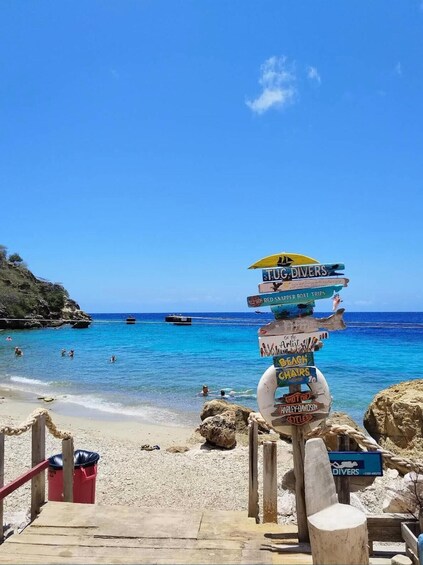 A beach with a signpost indicating activities like 'TUG DIVERS,' 'RED SNAPPER BOAT TRIPS,' and 'HARLEY-DAVIDSON CYCLES.' 3