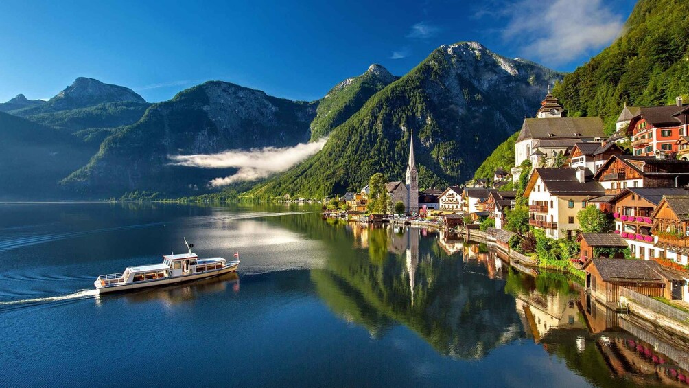A calm lake with a boat, a mountain range, and traditional buildings along the shore. 3