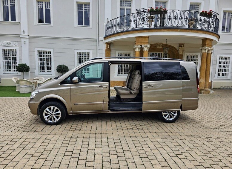 A beige van parked in front of a white building with a curved balcony and columns. 5