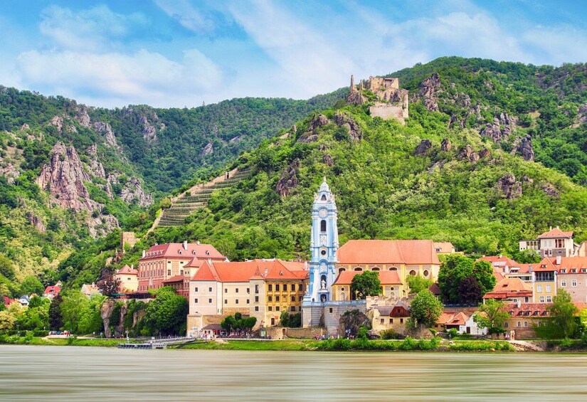 A town with a prominent clock tower, red-roofed buildings, and a castle on a hill. 4
