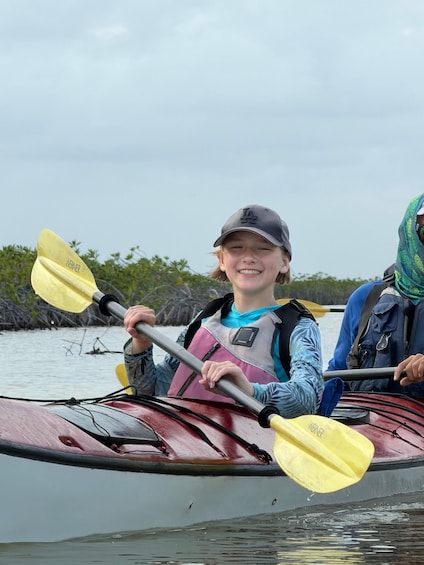 A person in a kayak with a life jacket, holding a paddle, and wearing a cap. 4