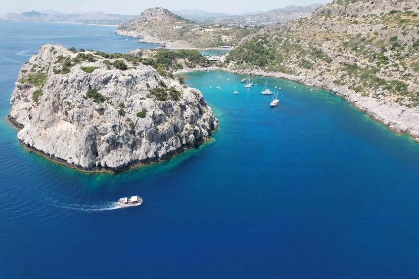 A rocky island surrounded by clear blue waters with several boats anchored nearby. 1