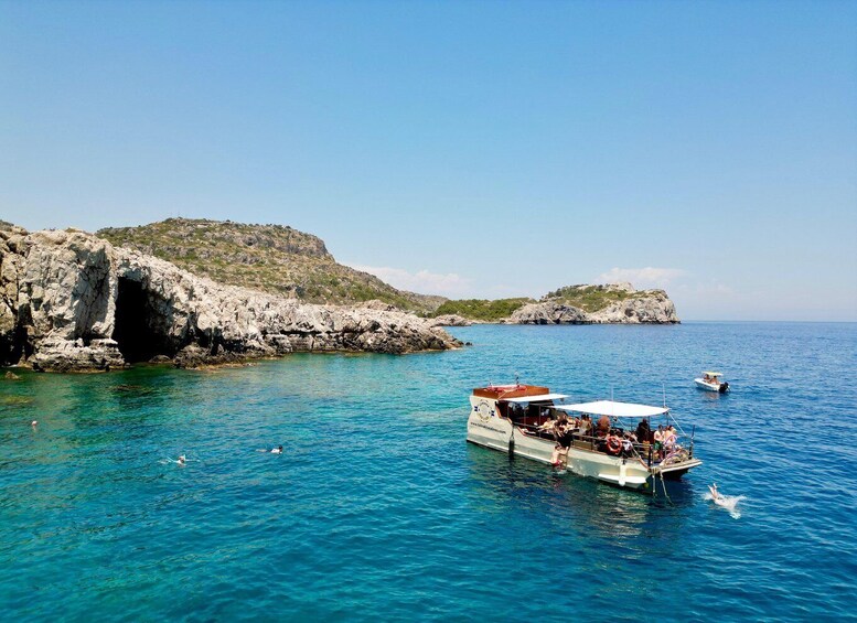 A boat with passengers, rocky coastline, clear blue sea, and distant islands. 3