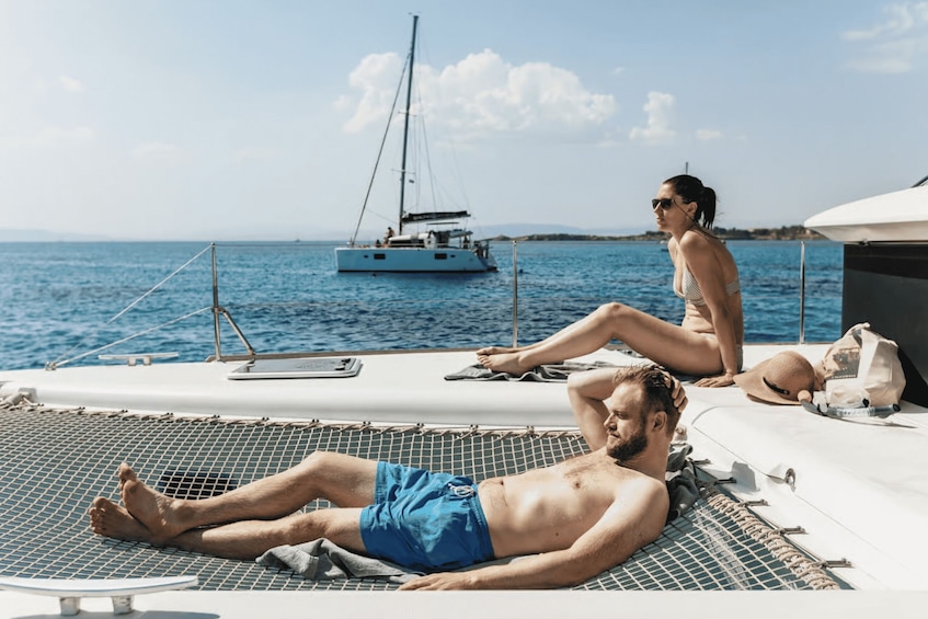 A man and a woman relaxing on a boat deck with a sailboat in the background. 5