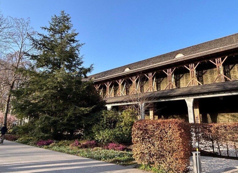 A building with a metal framework and a covered walkway, surrounded by trees and shrubs. 4