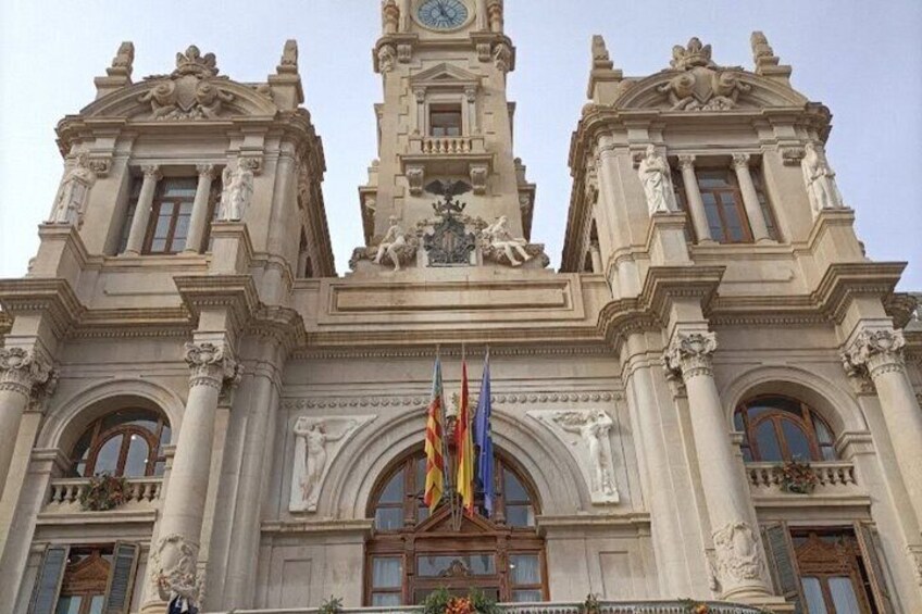 A grand building with a clock tower, columns, and flags. 1