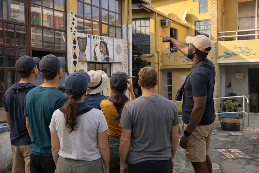 En gruppe mennesker står i et udendørs område med en bygning, der har et skilt med ordet 'Greeting' og et muralmaleri. 5