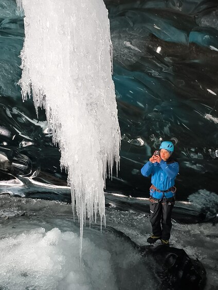 A person in blue gear standing near a large icicle formation in a cave. 5