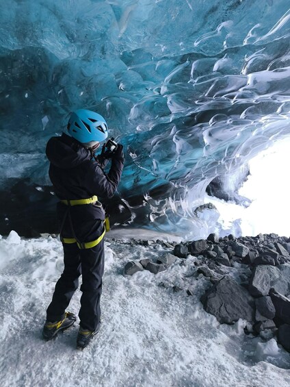 A person in a blue helmet and black and yellow gear taking a photo inside an ice cave. 1