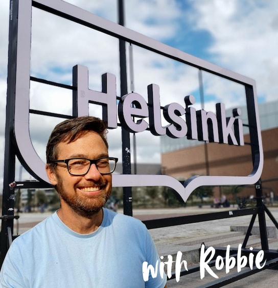 A person standing in front of a sign that reads 'Helsinki' with a clear sky in the background. 1