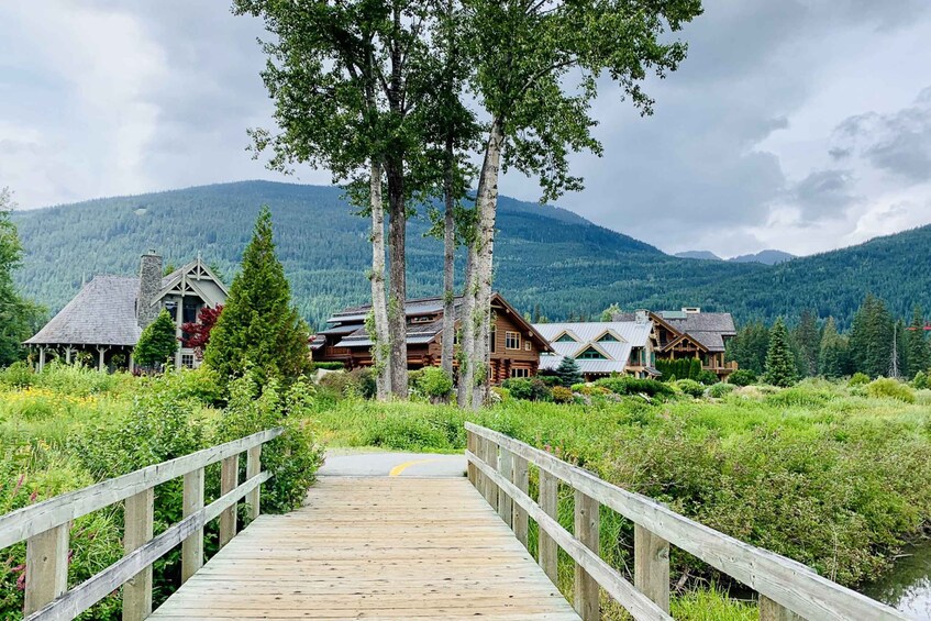 A wooden bridge leading to a lodge surrounded by forest and mountains. 2