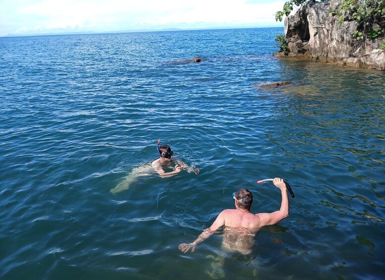 Two people swimming in a calm sea with rocky cliffs in the background. 3