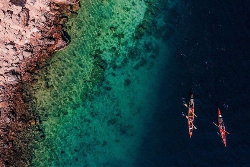 Two canoes on a clear turquoise sea with a rocky shoreline. 3