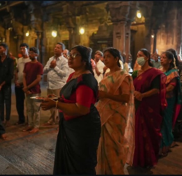 A group of people in traditional attire, standing in a dimly lit corridor with architectural columns. 4