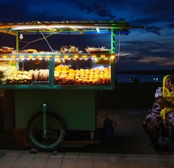 A food cart with various snacks and a person sitting nearby. 5