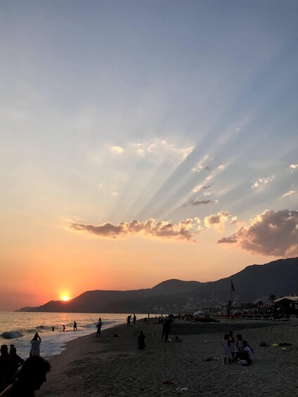 A beach at sunset with people walking and sitting, and a mountain in the background. 5