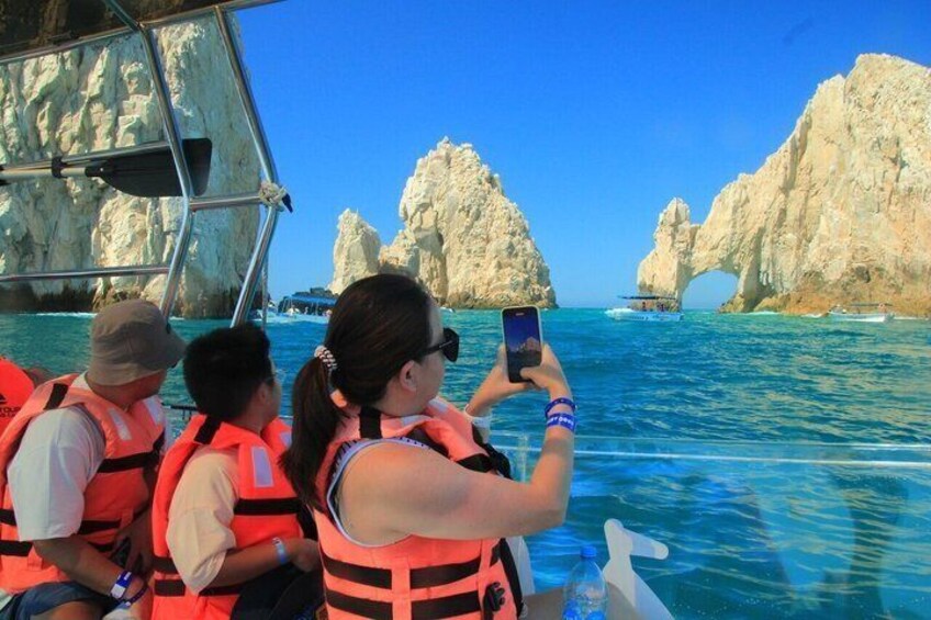 A boat with people wearing life jackets, a clear blue sea, and large rock formations in the background. 5