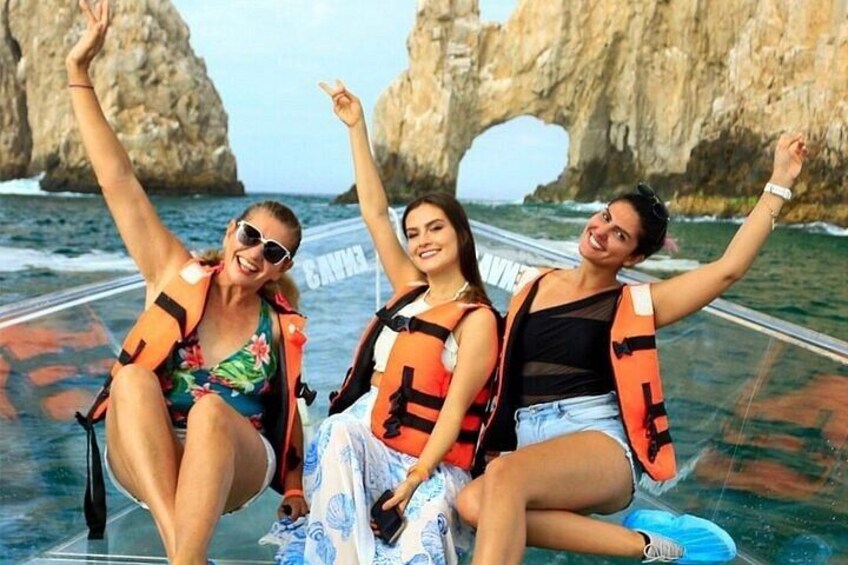 Three people on a boat, wearing life jackets, with a rocky coastline and a large rock formation in the background. 1