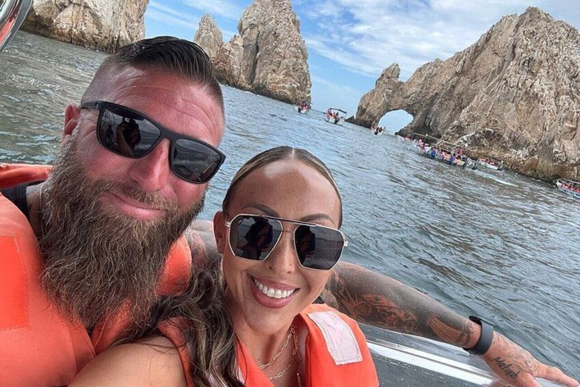 A boat with two people wearing life jackets, a rocky coastline, and a clear sky. 3