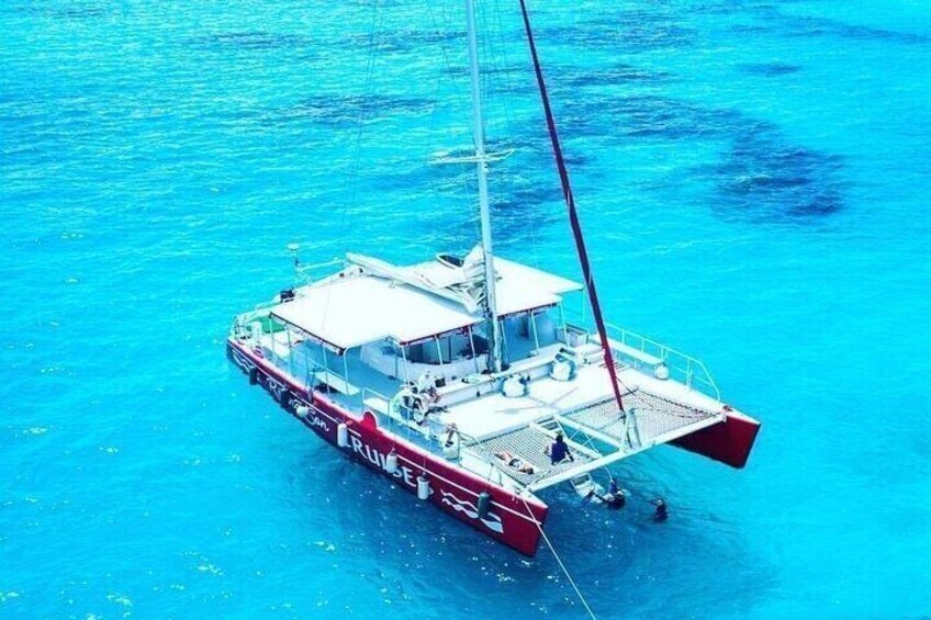 A red and white sailboat with a cabin and passengers on a clear blue sea. 5