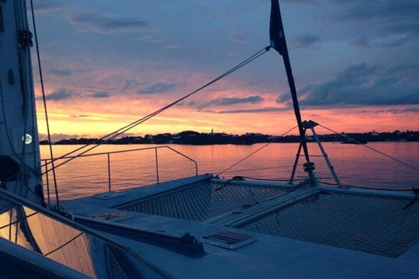 A sunset over calm waters with a boat deck and masts. 1