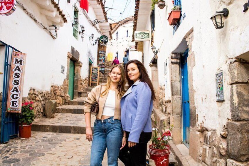 A narrow street with stone buildings, a massage sign, and a red bucket with flowers. 4
