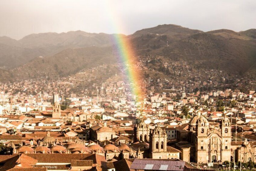 A cityscape with a prominent cathedral and a rainbow over mountains. 1