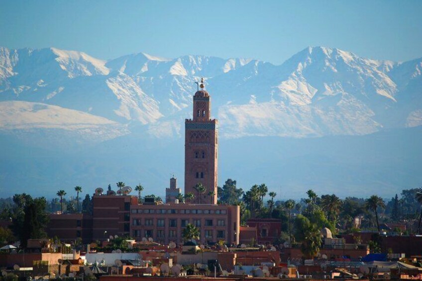 A historic building with a prominent tower, palm trees, and snow-capped mountains in the background. 1