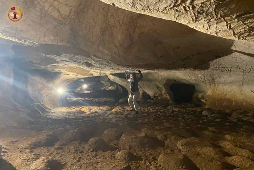 A person exploring a cave with a flashlight, surrounded by rocky terrain and cave walls. 5