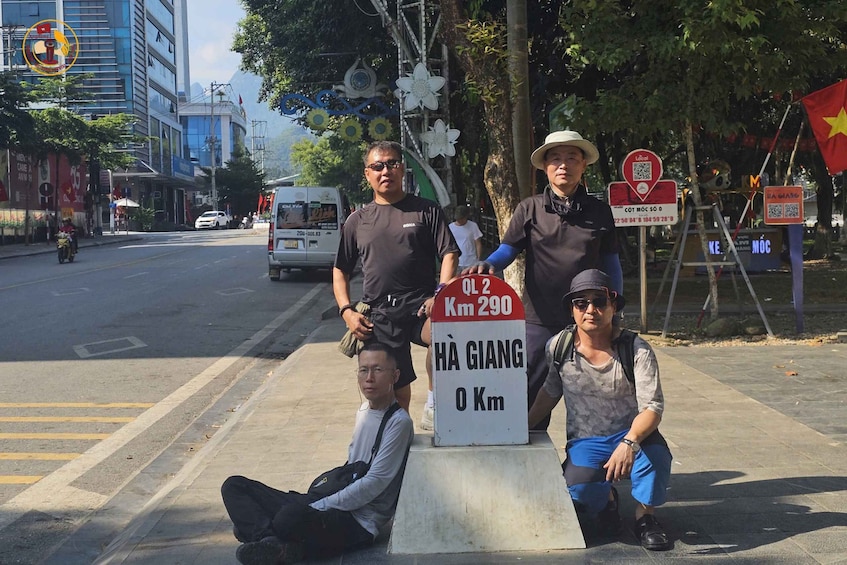 Three people posing with a sign indicating a distance of 290 km. 1