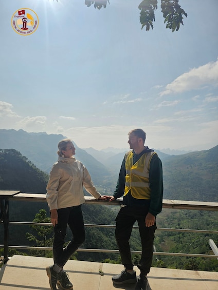Two people standing on a platform overlooking a mountainous landscape. 3