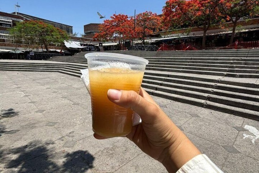 A hand holding a plastic cup with a beverage, a staircase, and buildings in the background. 2