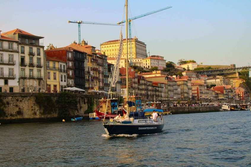 A sailboat on a river with buildings and a bridge in the background. 3
