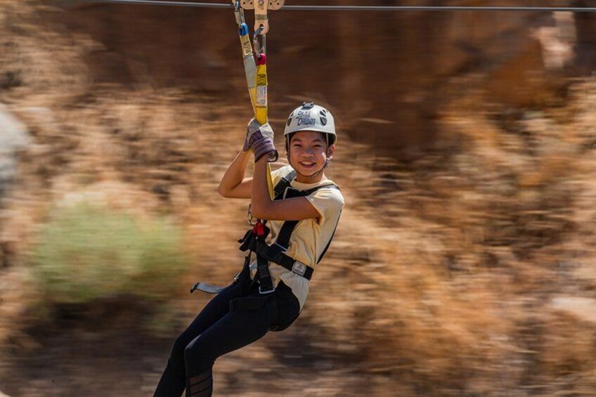 A person ziplining, wearing a helmet and harness, with a blurred natural landscape in the background. 3
