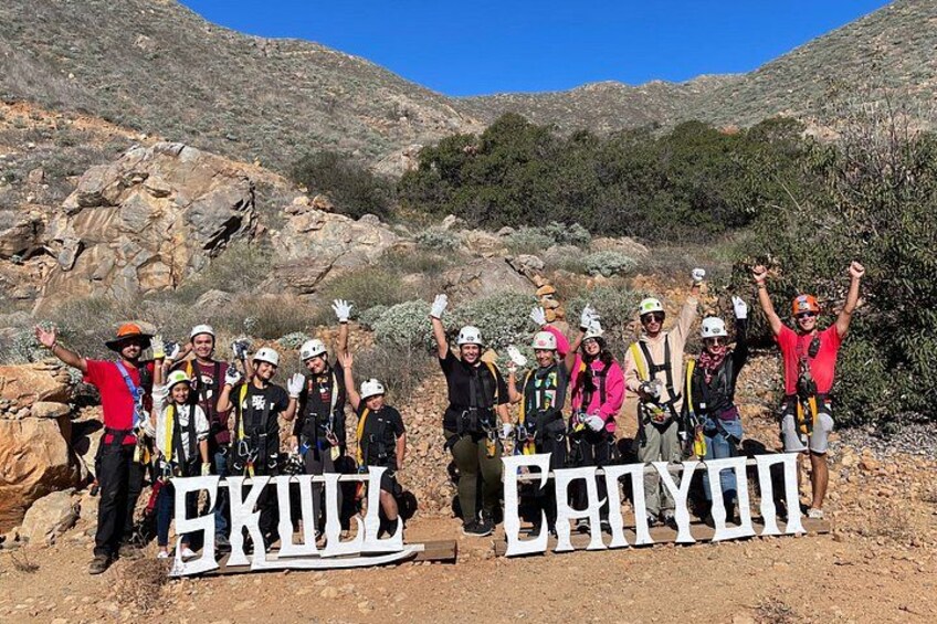 A group of people with backpacks and helmets, standing in a rocky outdoor area with a clear sky. 5
