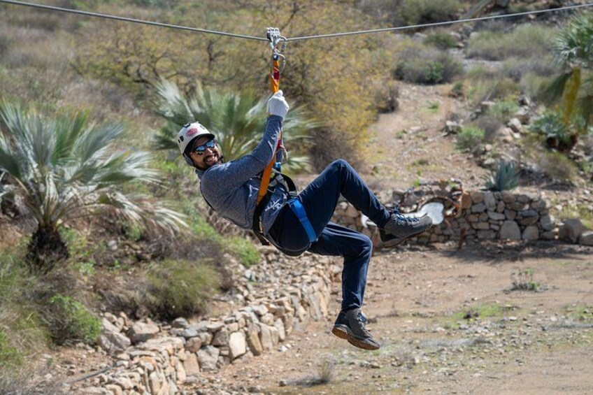A person zip-lining through a natural landscape with rocky terrain and sparse vegetation. 2