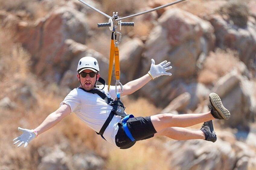 A person ziplining with a harness and safety gear, suspended in mid-air with a rocky landscape in the background. 4