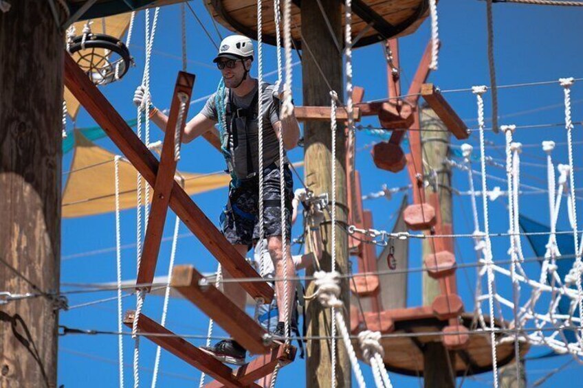 A person navigating a rope course with wooden structures and ropes. 2