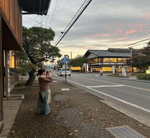 A person taking a photo on a city street with traditional architecture and a pedestrian crossing sign. 2