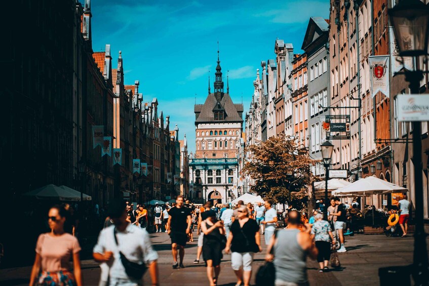 A bustling street with historic buildings, a prominent church tower, and outdoor market stalls. 5