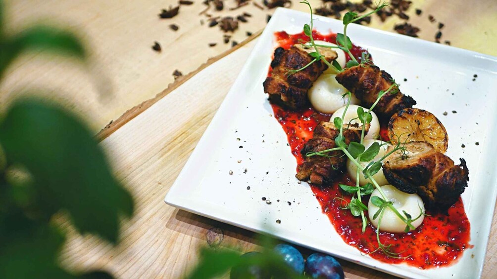 A white plate with grilled meat, round slices of potato, and a red sauce, garnished with microgreens, on a wooden table. 4