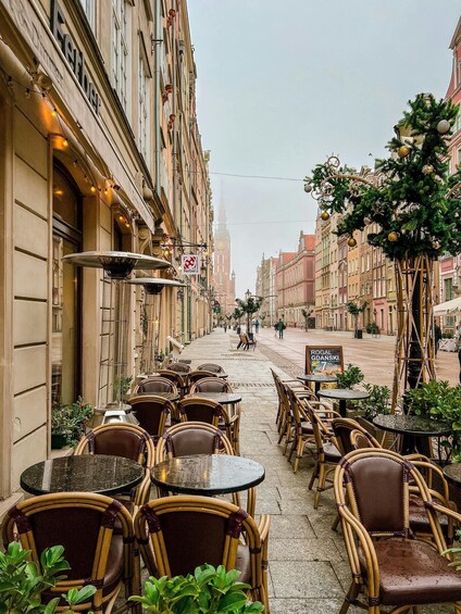 Outdoor cafe seating with wicker chairs and tables, a street with buildings, and a Christmas tree with ornaments. 2