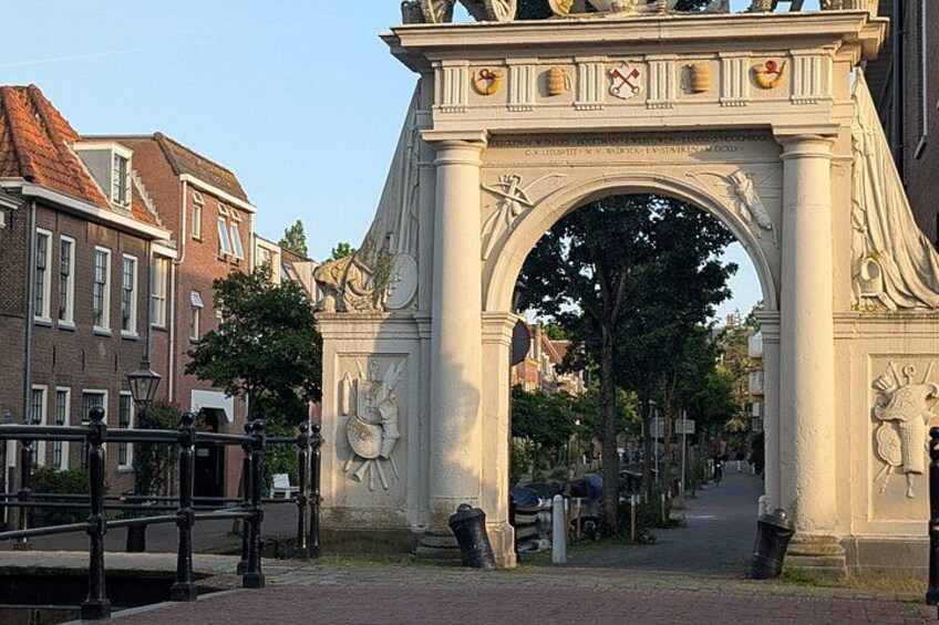 A historic archway with intricate carvings and a clock, surrounded by traditional buildings and a cobblestone path. 5